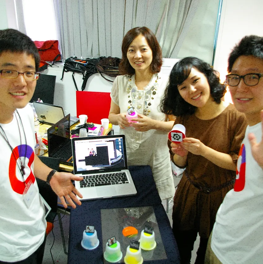 A hackathon team of 2 women and 2 men smiling over a tabletop interface